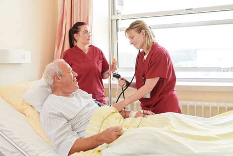 Zwei Pflegerinnen messen bei einem Patienten den Blutdruck