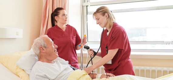 Zwei Pflegerinnen messen den Blutdruck eines älteren Patienten