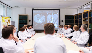 Besprechung an der Klinik für Urologie: Alle Ärzte haben sich um einen großen Tisch versammelt und besprechen den Röntgenbefund eines Patienten. Der Befund ist auf dem Monitor zu sehen.